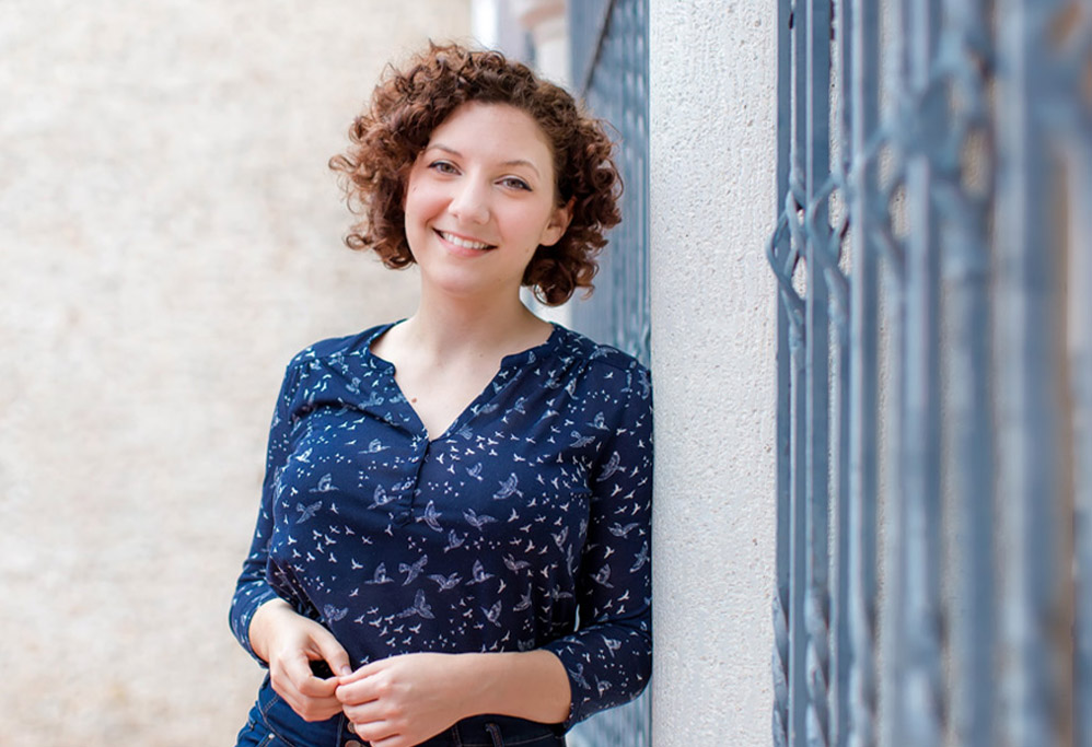 Woman with curly hair leaning on a wall smiling at the camera